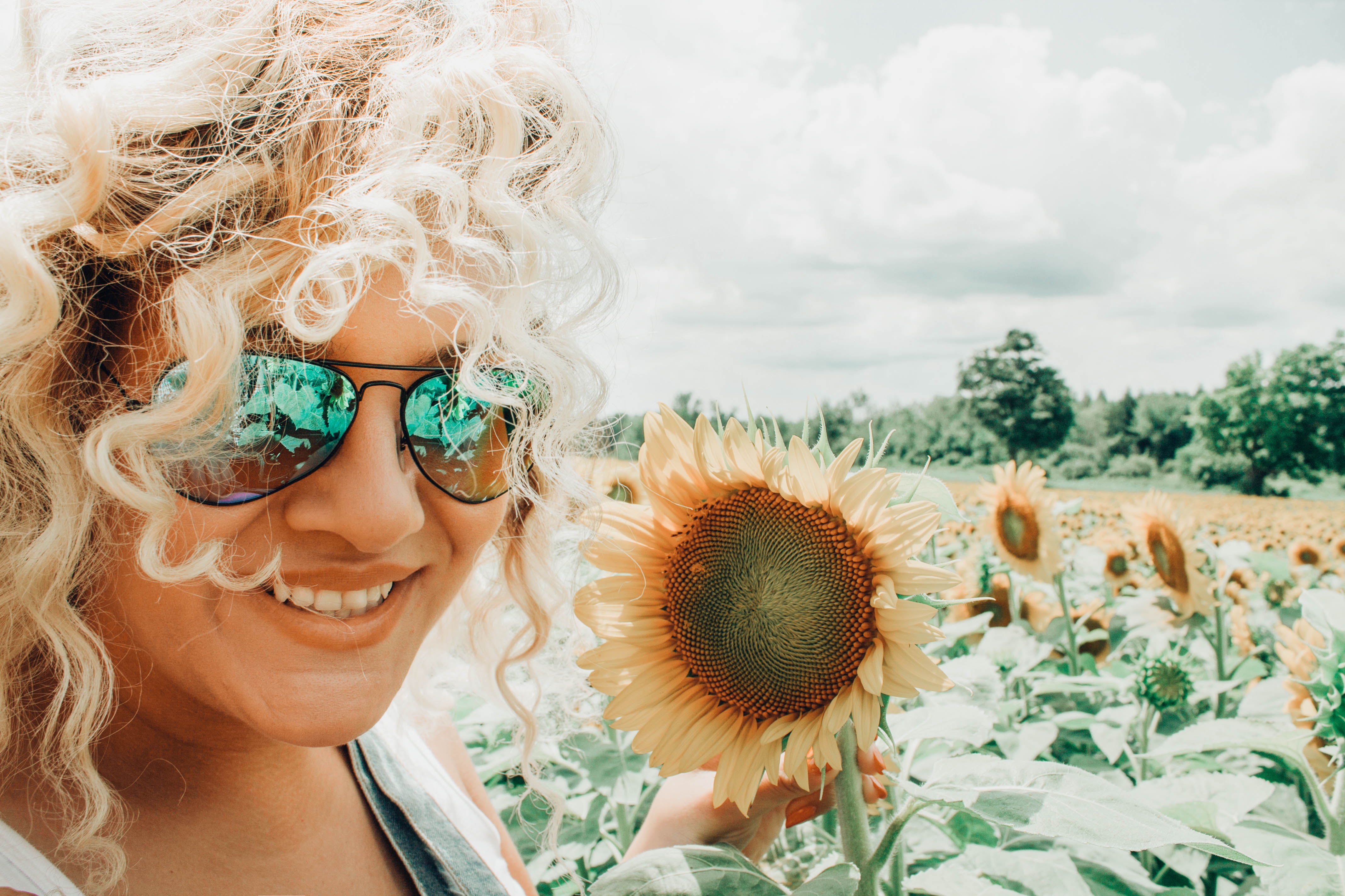 Woman with curly haistyle is taking her selfie with the sunflowers